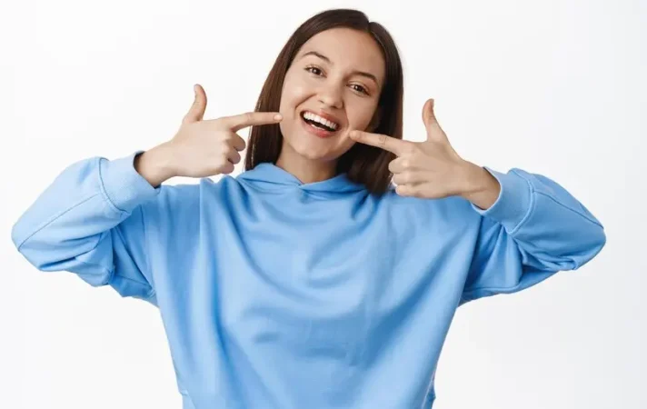 happy-girl-pointing-fingers-white-perfect-smile-straight-whitened-teeth-standing-hoodie-against-white-background